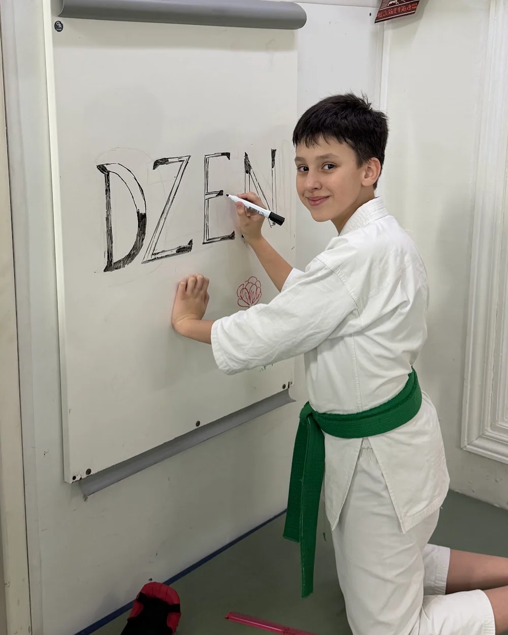 Учень DZEN KARATE CLUB у кімоно пише на дошці слово DZEN